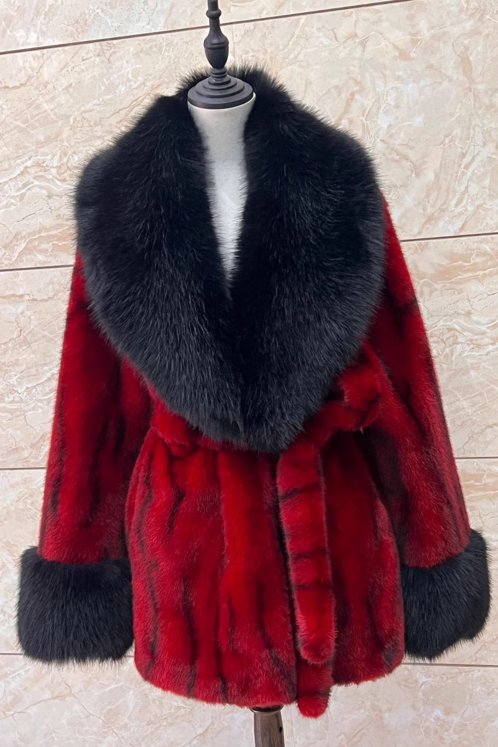 Red fur coat with black fur collar on a mannequin against a beige tiled wall.