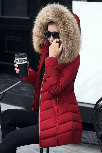 Person wearing a red puffer jacket with a fur hood, sitting outdoors holding a coffee cup.