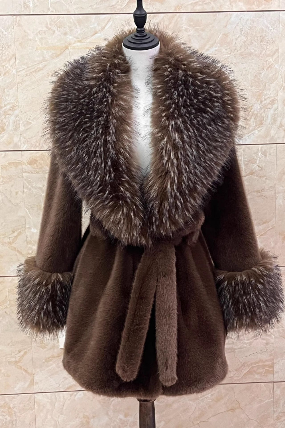 Brown coat with fur collar on a mannequin against a beige tiled wall.