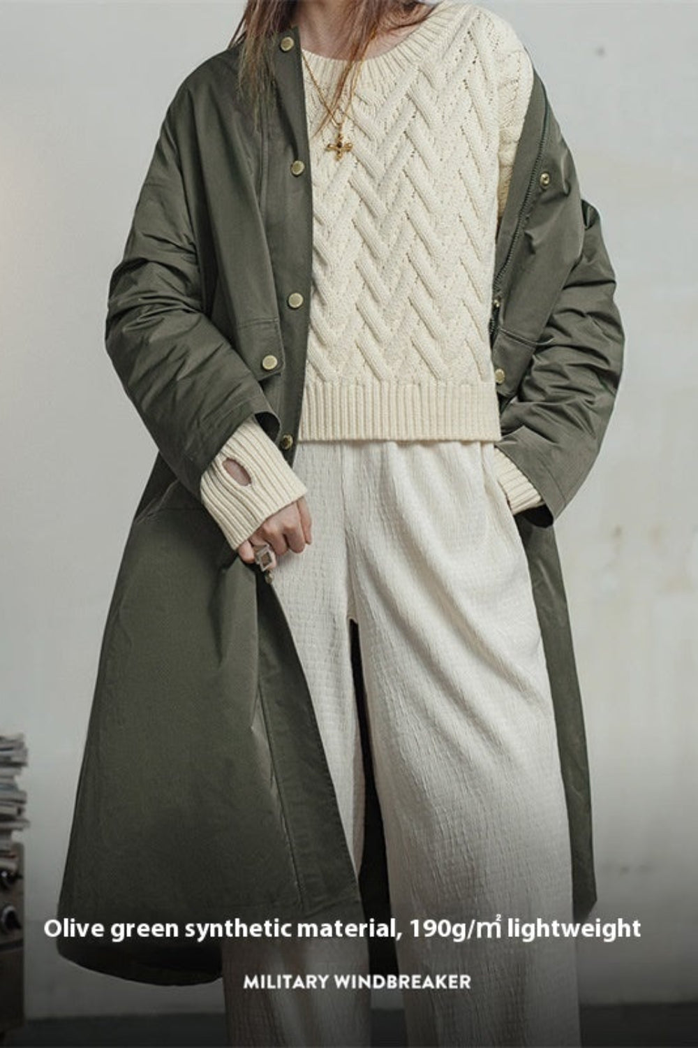 Person wearing a long olive green military-style jacket over a cream sweater and pants, with text about material and weight.