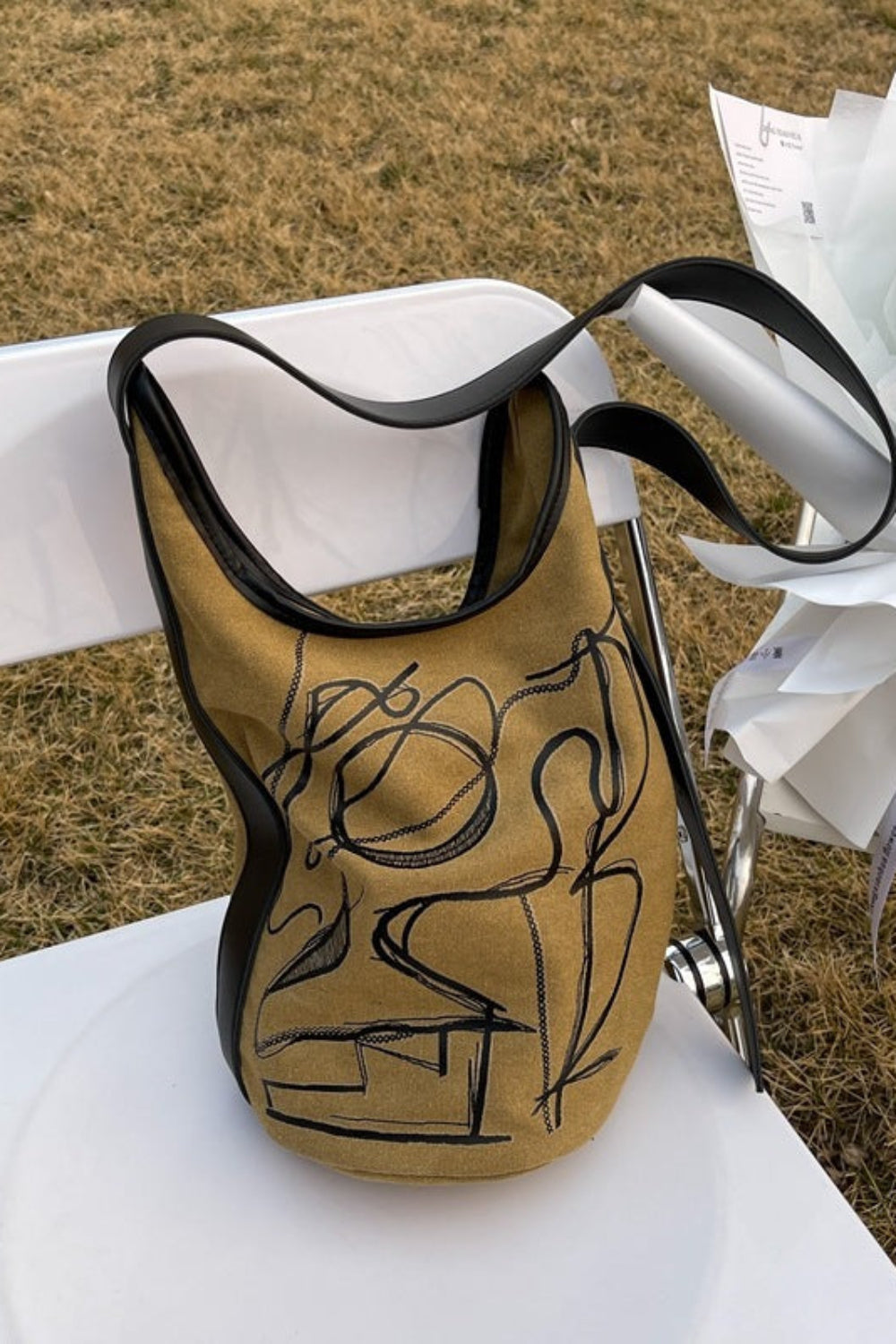 Gold and black bag with artistic design on a white chair outdoors