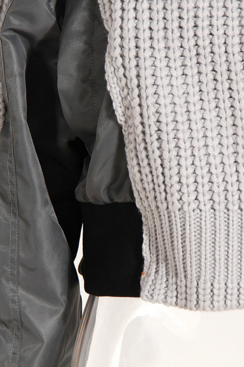 Close-up of a gray knit sweater with a black jacket underneath on a white background