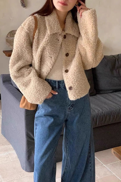 Person wearing a beige sherpa jacket and blue jeans standing in a living room.
