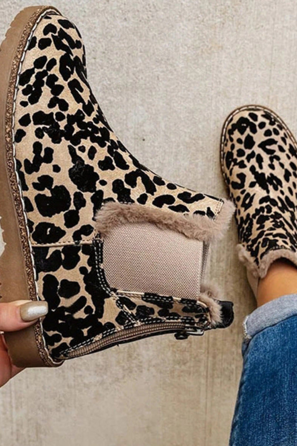 Leopard print boots with fur lining held by a hand on a neutral background
