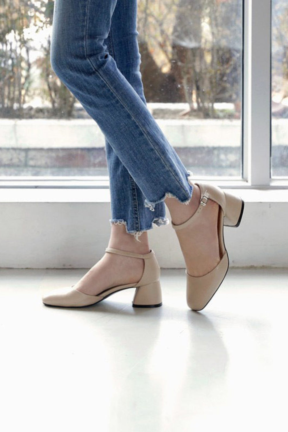 Person wearing beige shoes and blue jeans standing in front of a window.