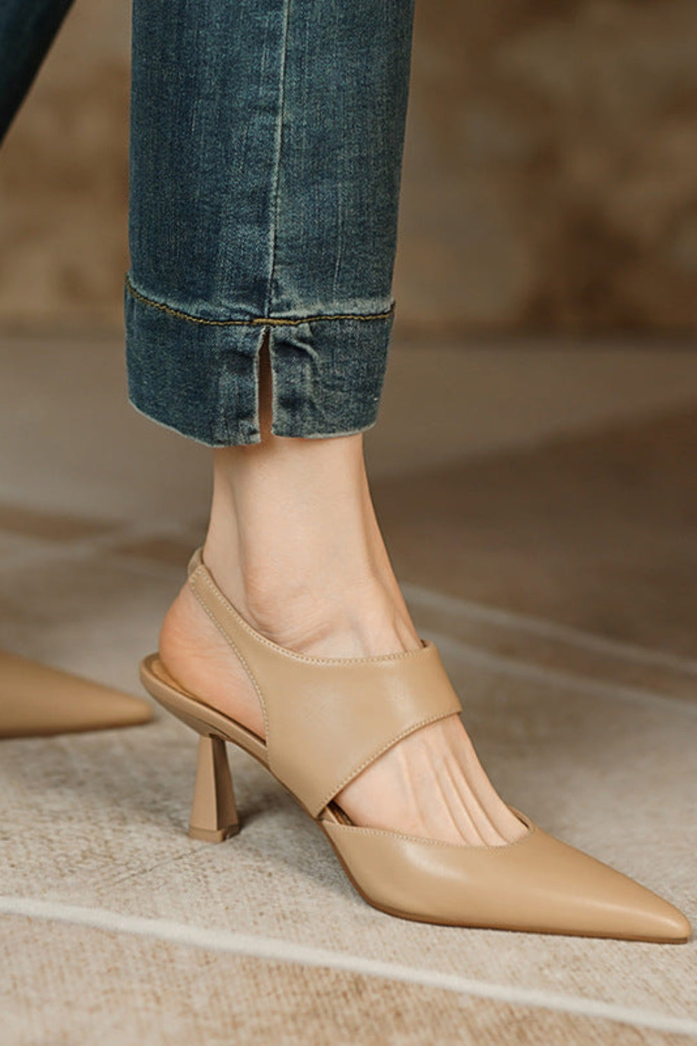 Beige high-heeled shoes worn with rolled-up jeans on a neutral background
