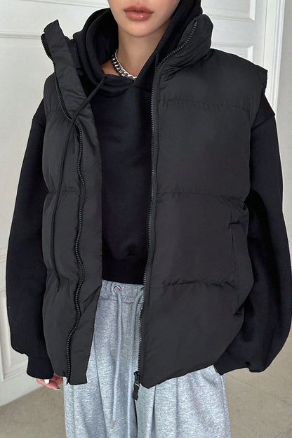 Person wearing a black puffer vest over a black shirt and light gray pants indoors.