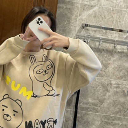 Person wearing a beige sweatshirt with cartoon designs and text, taking a mirror selfie.