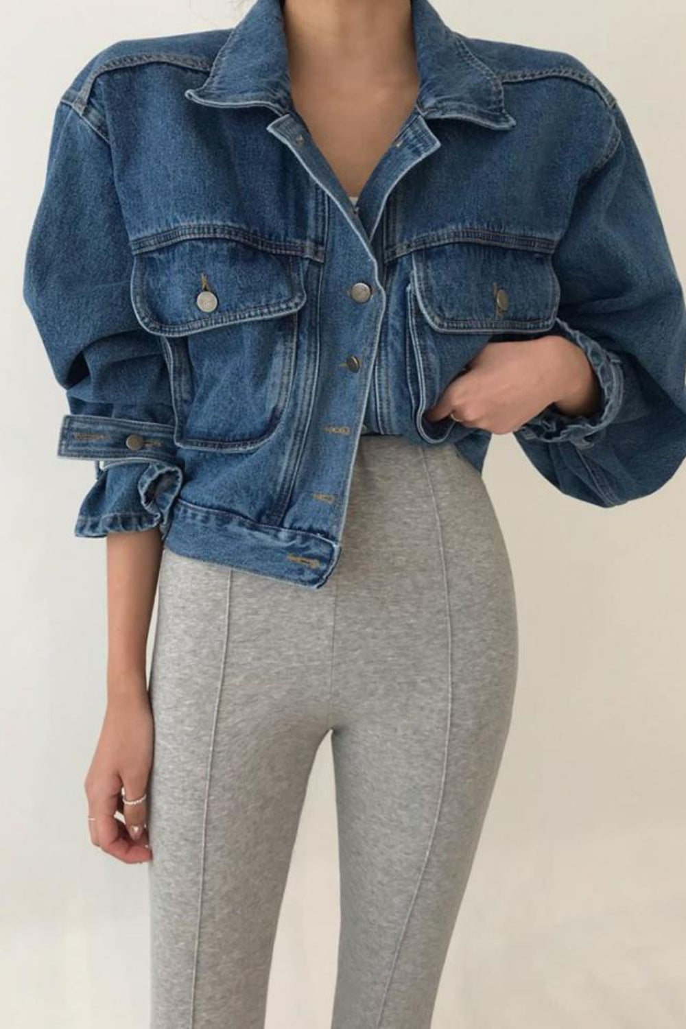 Person wearing a blue denim jacket and gray pants on a plain background