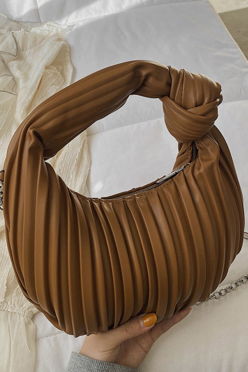 Brown pleated handbag with a knotted handle held by a hand on a light background