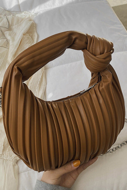 Brown pleated handbag with a knotted handle held by a hand on a light background