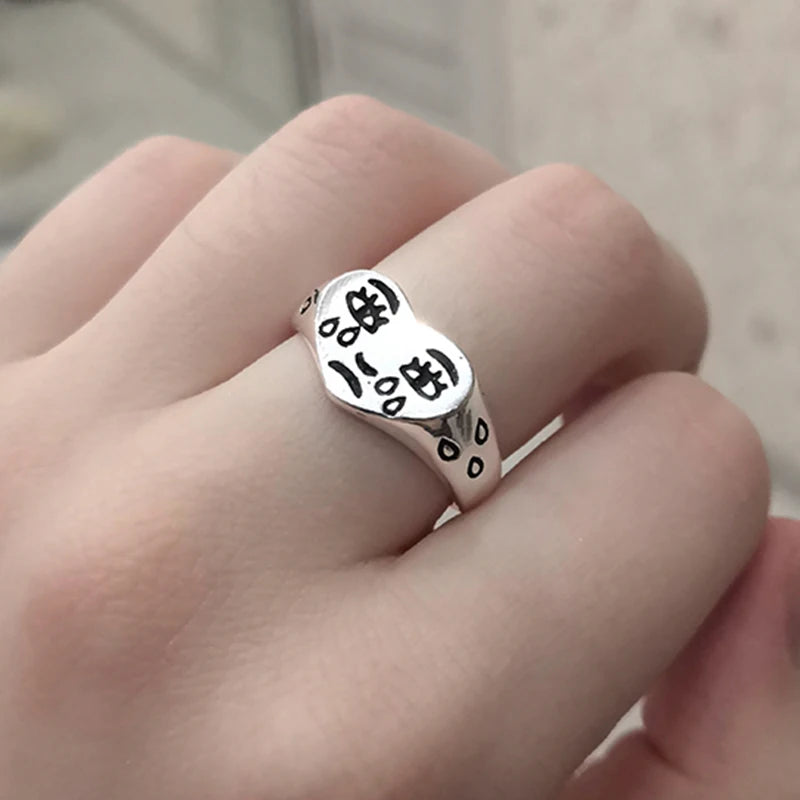 Silver ring with black text on a finger against a neutral background