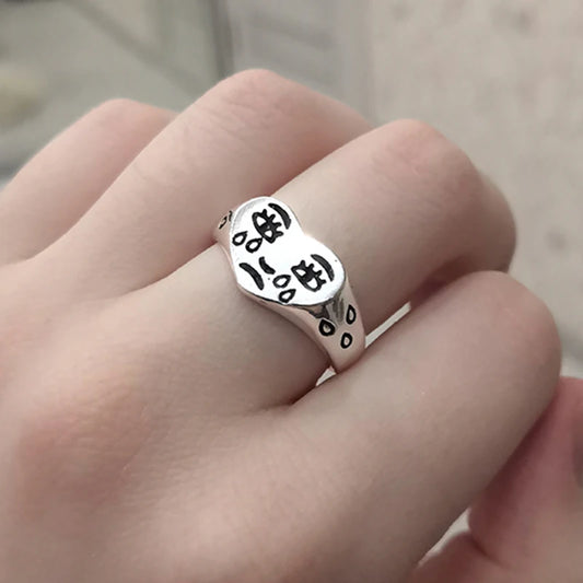 Silver ring with black text on a finger against a neutral background