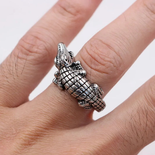 Silver alligator-shaped ring on a person's finger with a white background