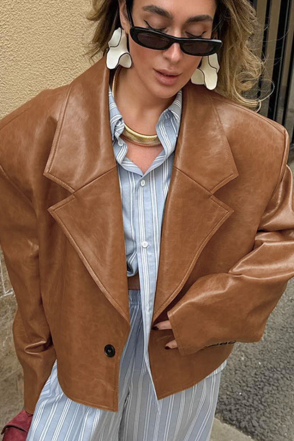 Person wearing a brown leather jacket and striped shirt against a beige wall.