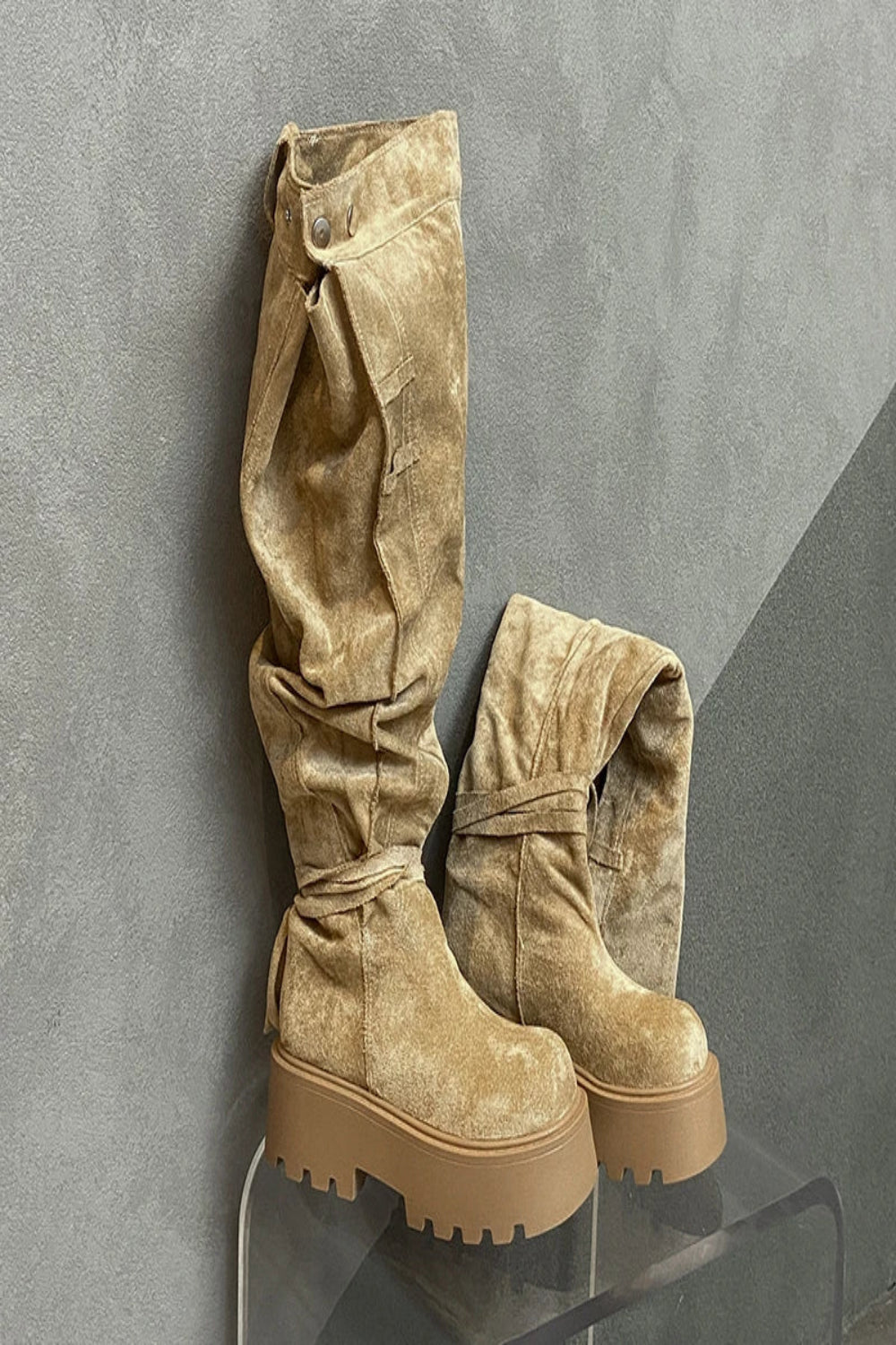 Pair of beige suede boots on a gray surface with a gray background