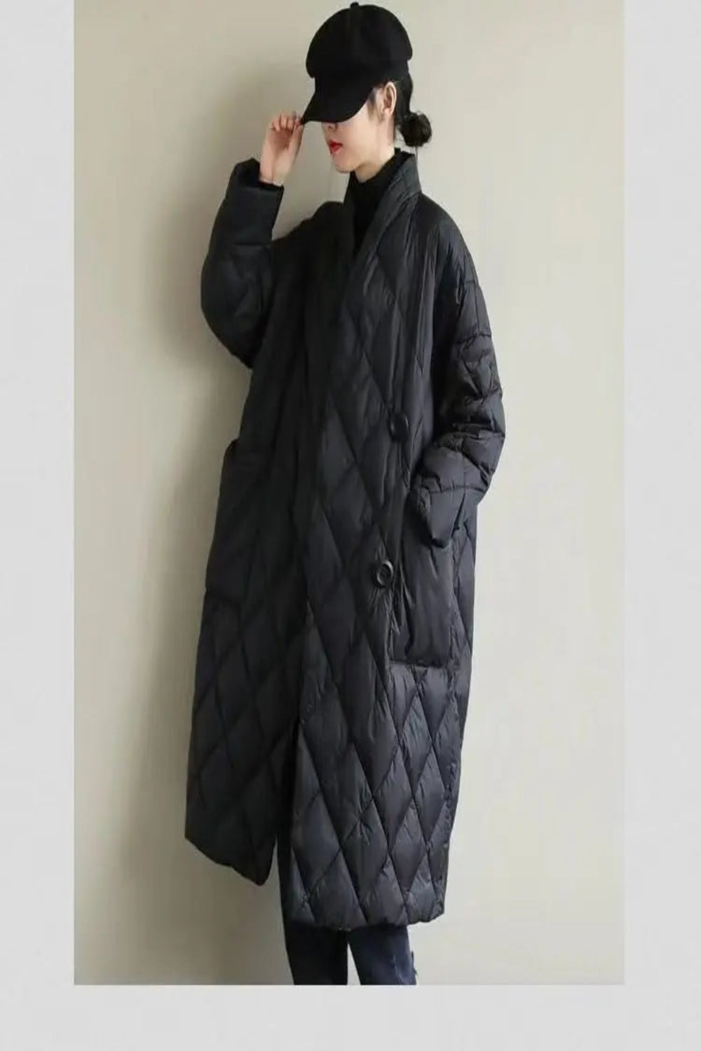 Person wearing a long black quilted coat against a plain background