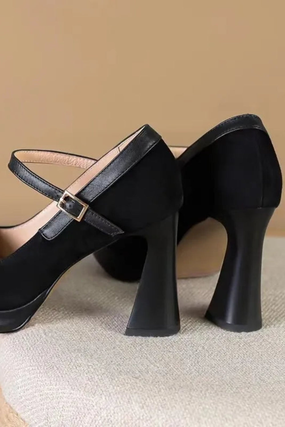 Black high-heeled shoes with a strap on a beige surface and background