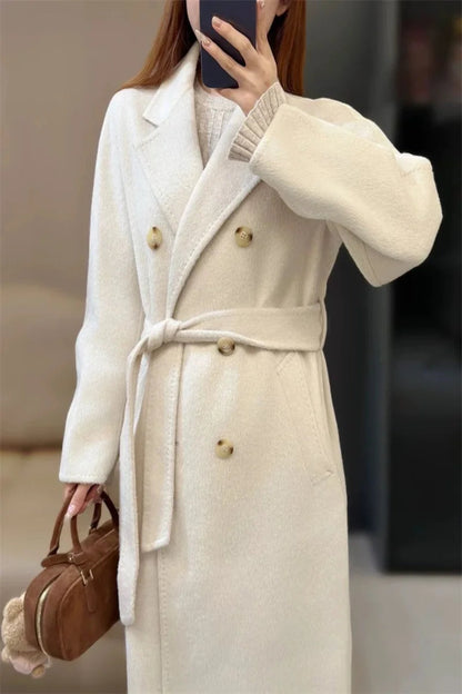 Person wearing a long beige coat with a belt, holding a brown handbag.