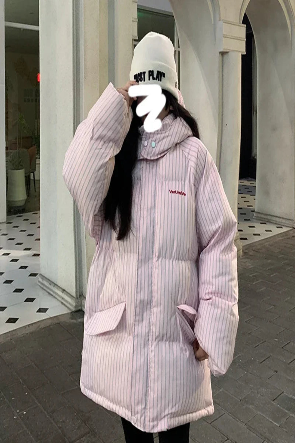 Person wearing a light pink puffer jacket with a brand logo, standing in an outdoor setting.