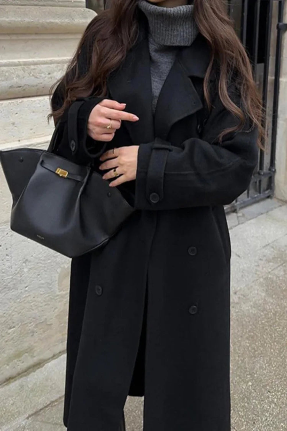 Person wearing a black coat holding a black handbag on a street.