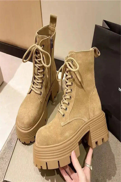Tan platform boots with a person's hand holding one of them on a neutral background