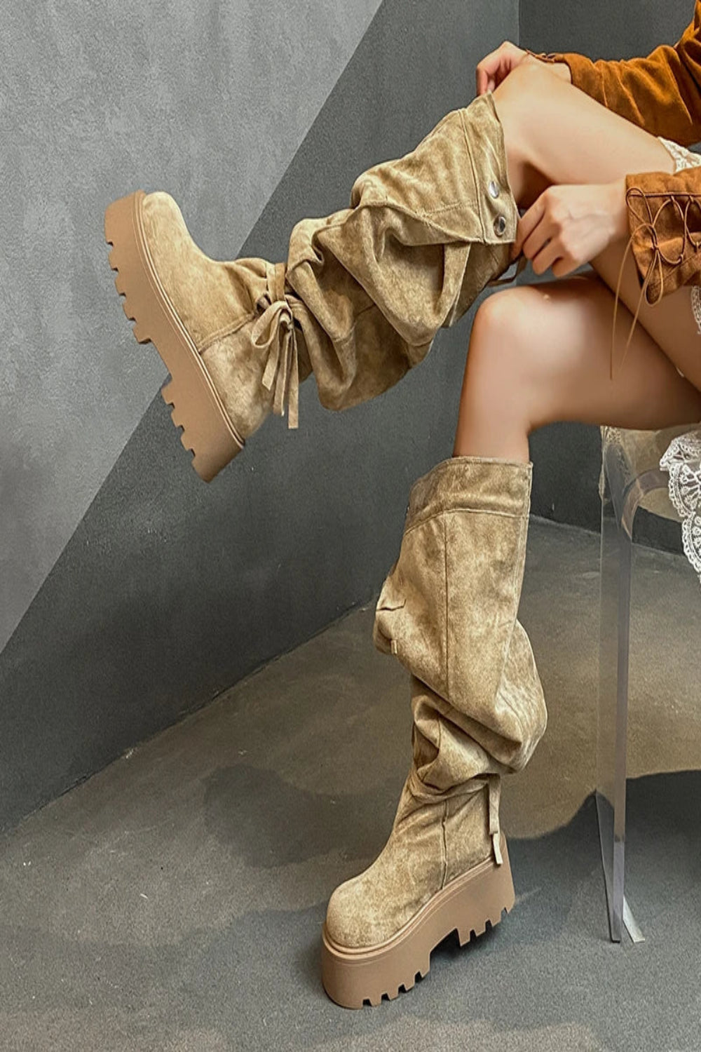 Person wearing beige suede knee-high boots with a gray background