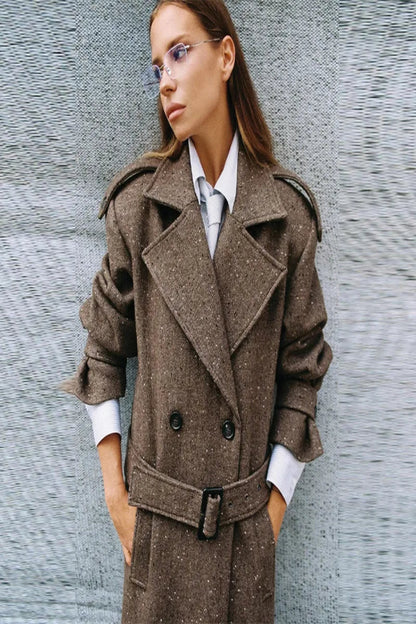Woman wearing a brown trench coat against a textured gray wall