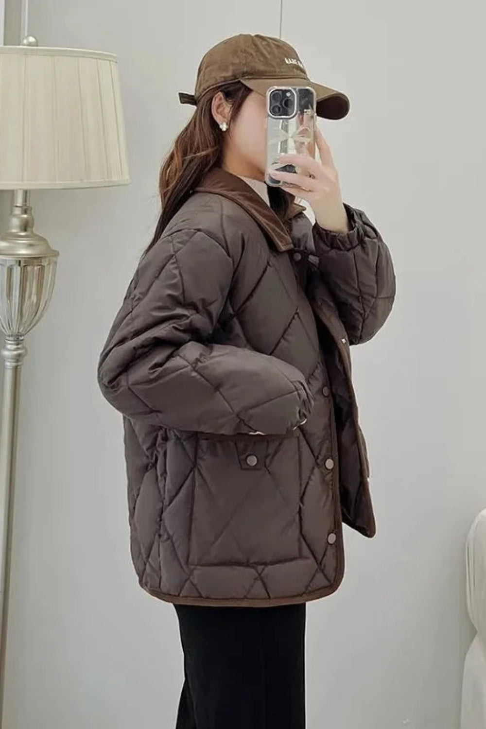 Person wearing a brown quilted jacket and cap taking a mirror selfie.