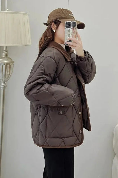 Person wearing a brown quilted jacket and cap taking a mirror selfie.