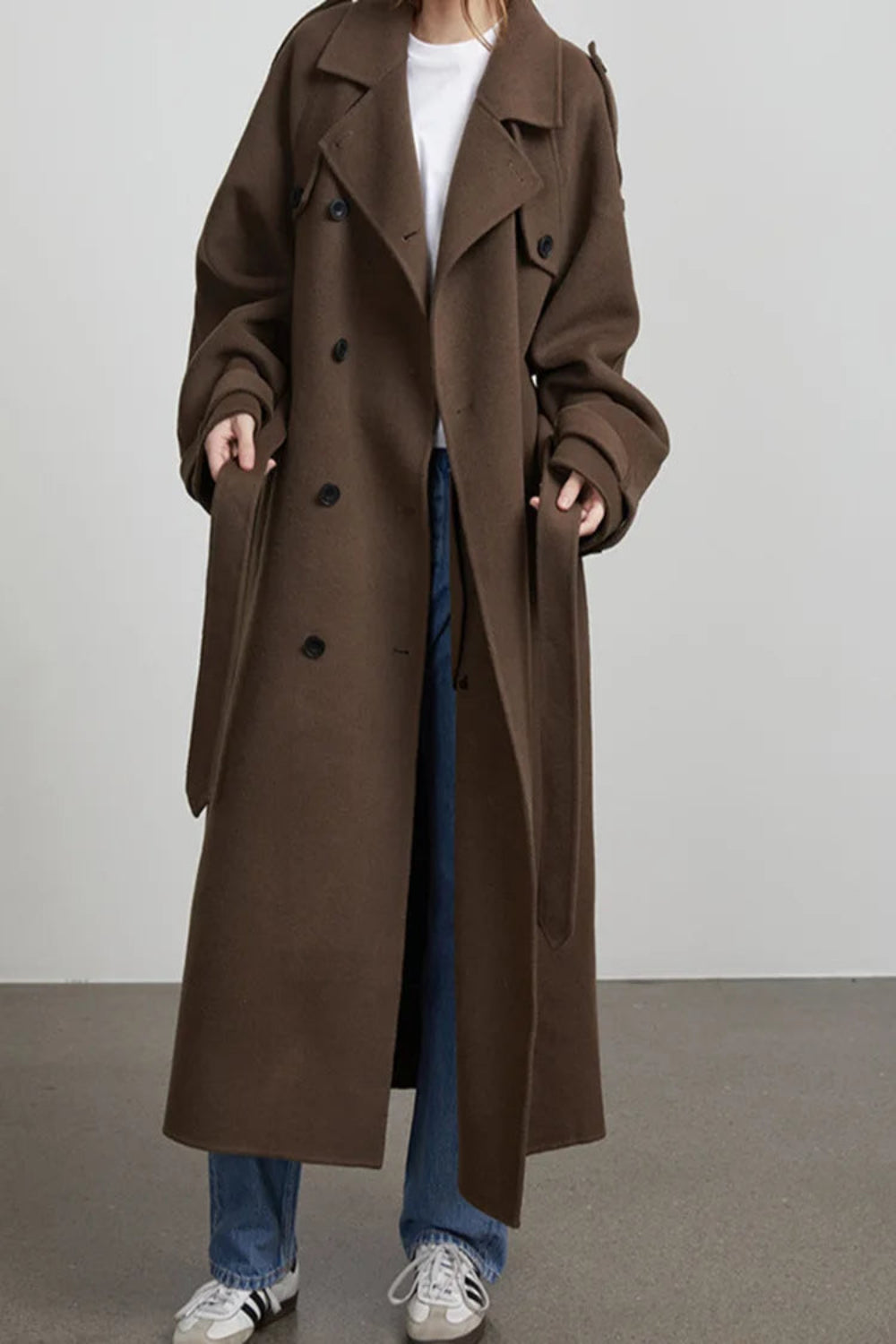 Person wearing a long brown coat with a plain background