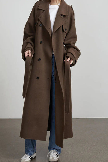 Person wearing a long brown coat with a plain background