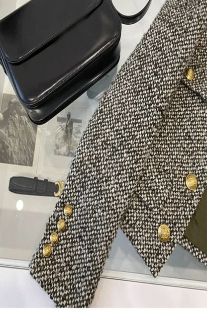 Black leather clutch bag and textured coat with gold buttons on a reflective surface.