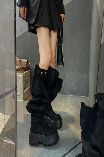 Person wearing black platform boots with a reflective surface and gray floor.