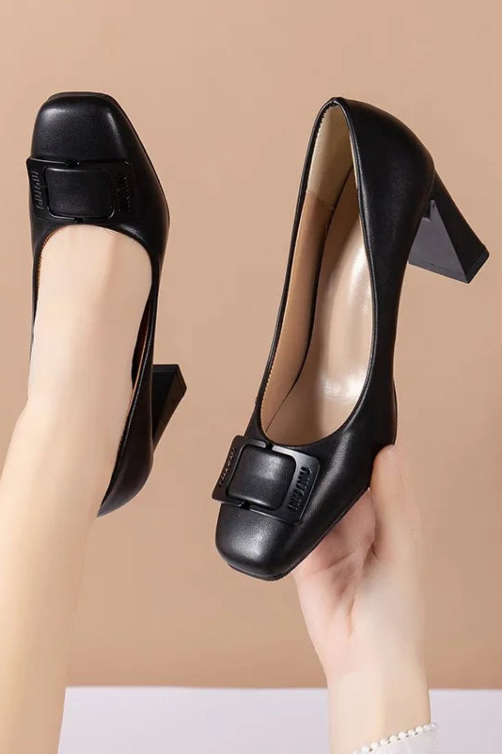 Black high-heeled shoes with a square toe and buckled design on a beige background