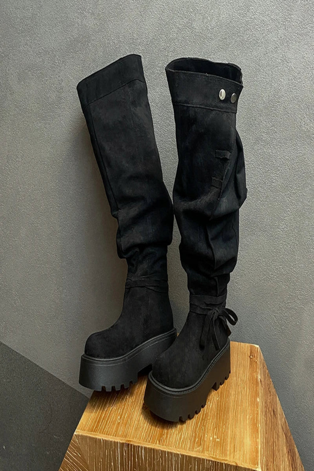 Black platform boots on a wooden block against a gray background