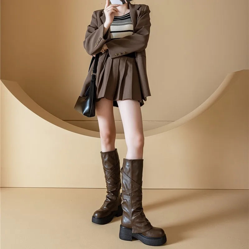 Person wearing a brown outfit with a skirt and knee-high boots against a beige background