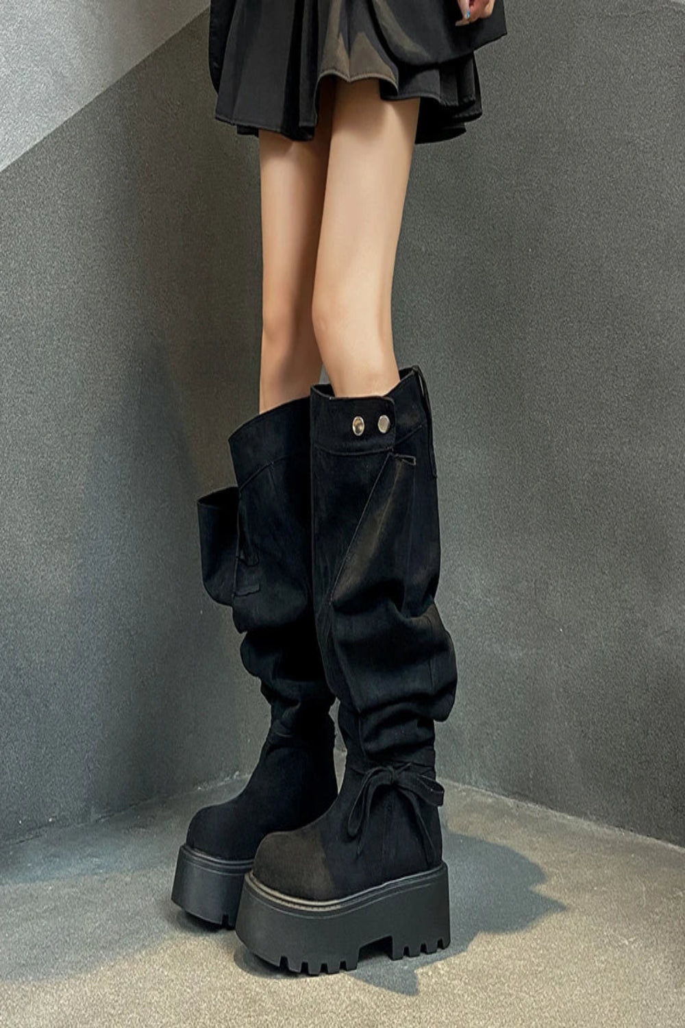 Black knee-high boots worn with a black skirt against a gray background