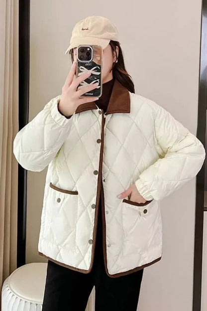Person wearing a white quilted jacket with brown accents taking a mirror selfie.