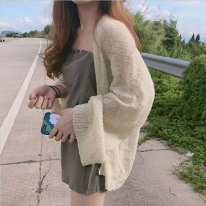 Person wearing a beige cardigan over a green dress on a road with greenery in the background