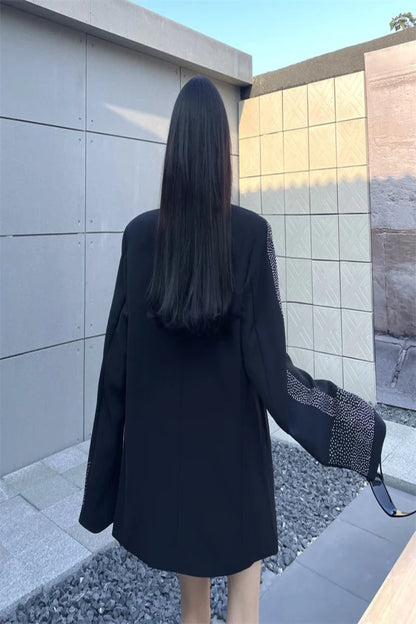 Person wearing a black outfit with patterned sleeves standing in front of a modern building.