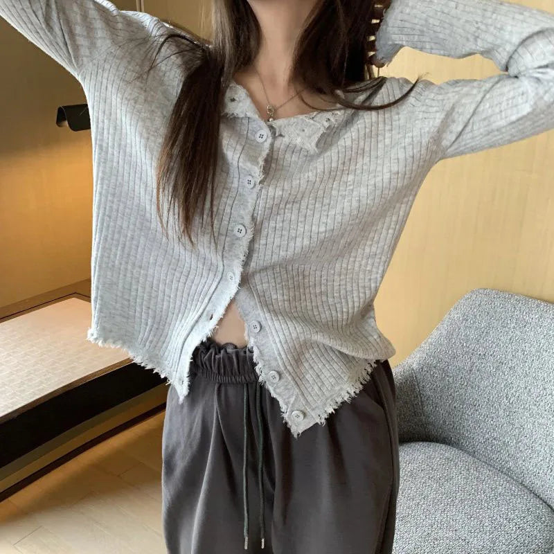 Person wearing a light gray textured cardigan over a white shirt with dark pants, standing indoors.