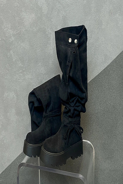 Black platform boots with high legs on a clear stool against a gray background