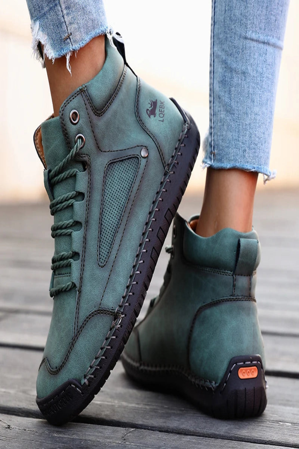 Teal high-top sneakers with black soles worn by a person on a wooden floor.