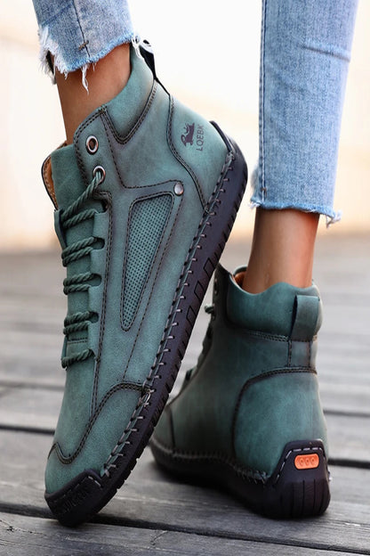 Teal high-top sneakers with black soles worn by a person on a wooden floor.
