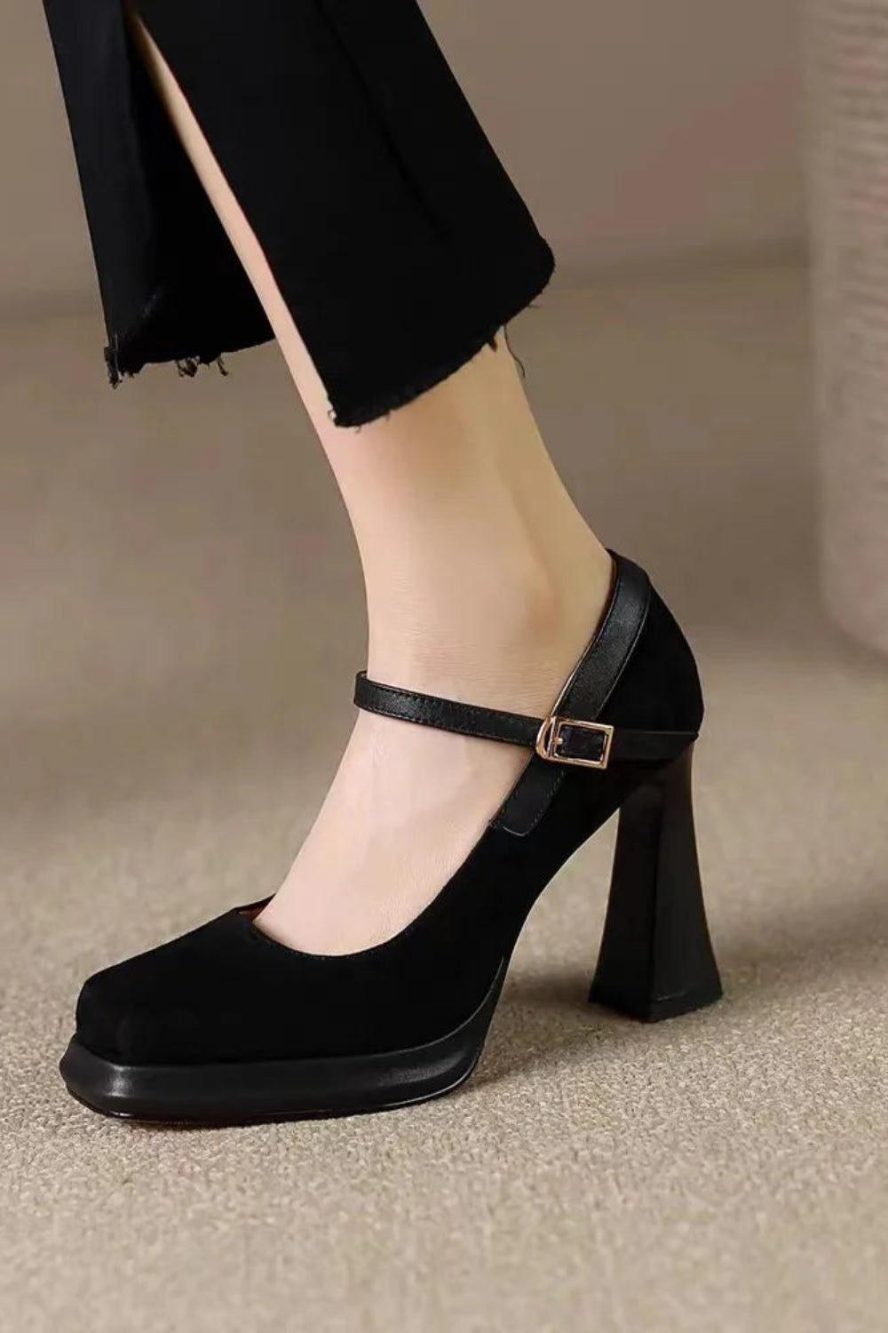 Black high-heeled shoes with a strap worn by a person on a neutral background