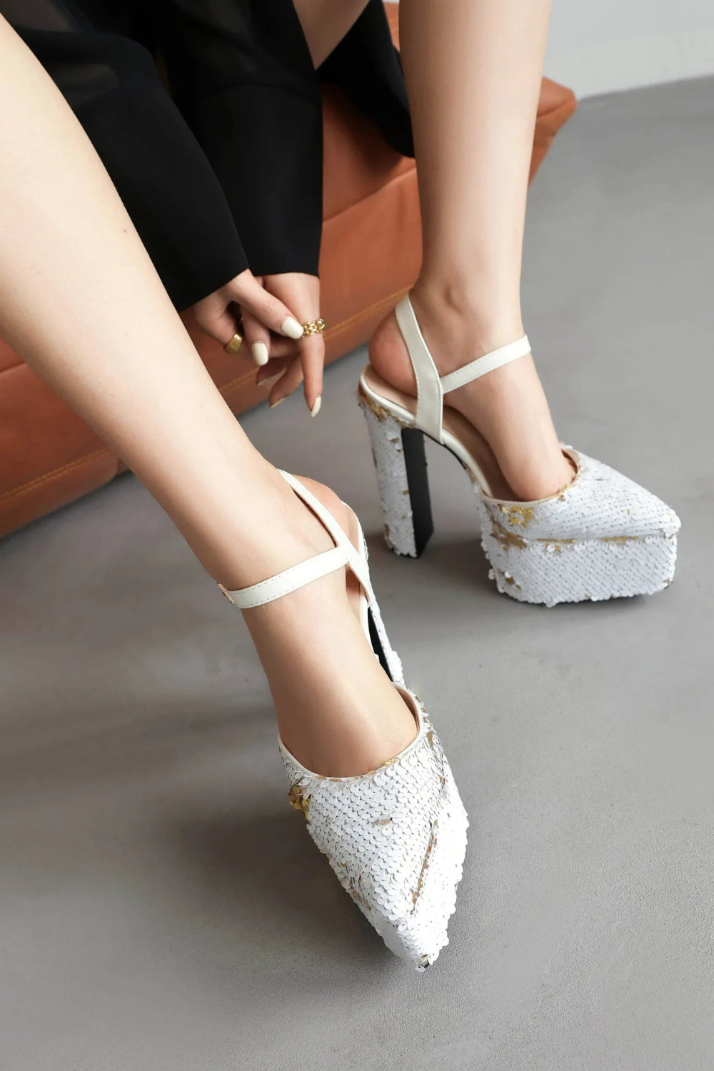 White platform heels with gold accents worn by a person sitting on a couch.