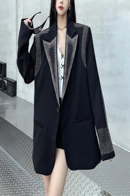 Person wearing a black blazer with decorative elements on a metallic floor.