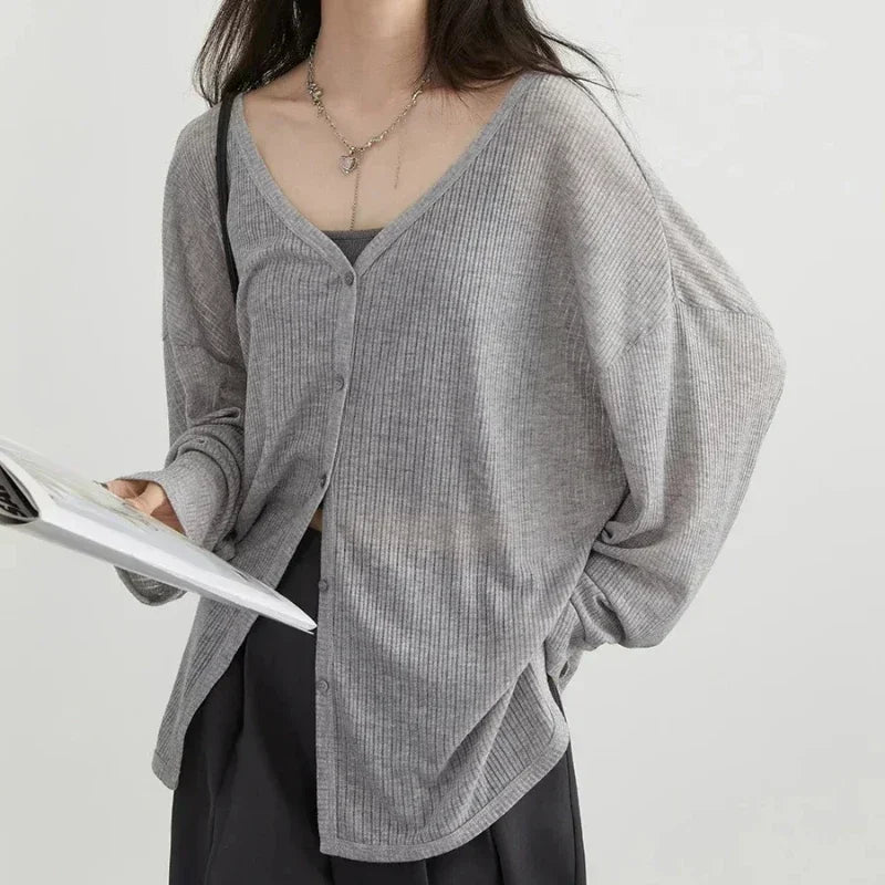 Person wearing a gray ribbed cardigan over a black top on a light gray background