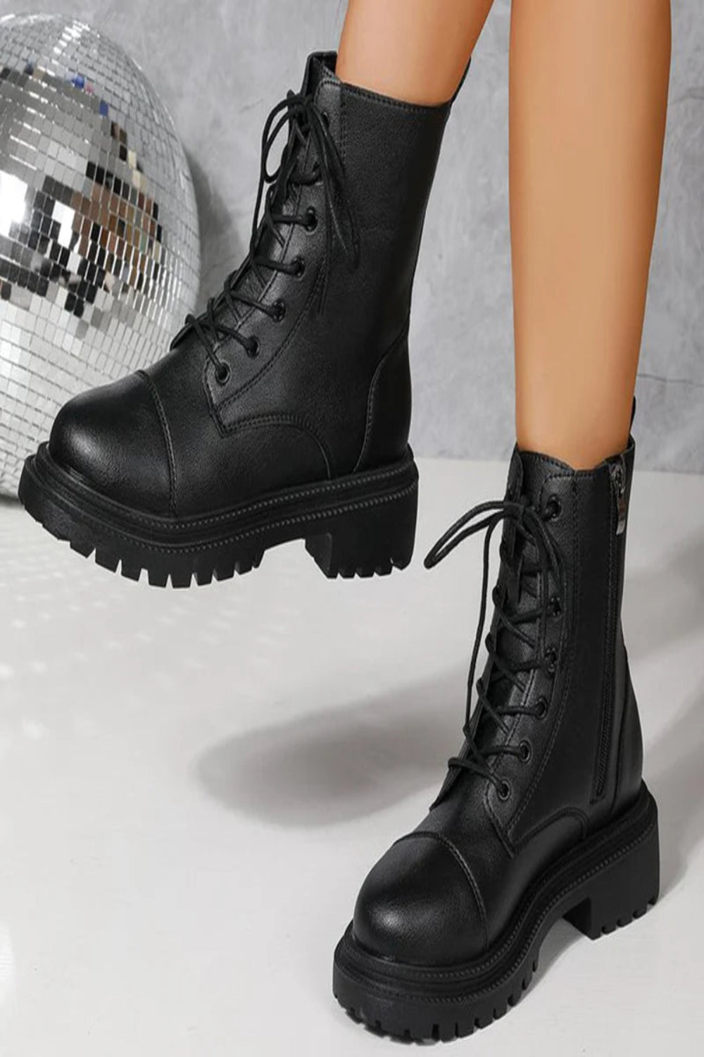 Black leather boots worn by a person with a disco ball in the background